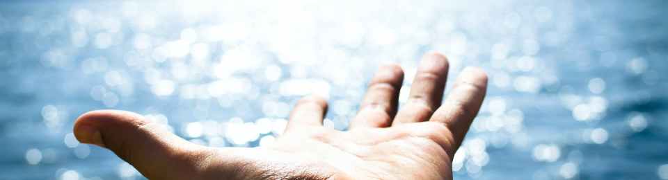 person hand reaching body of water